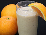 Orange smoothie in a glass next to two oranges