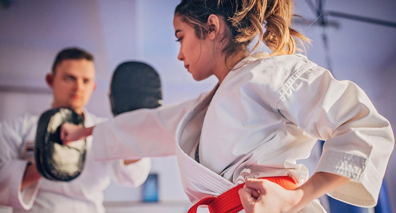 Young female karate player with trainer using focus mitts during training