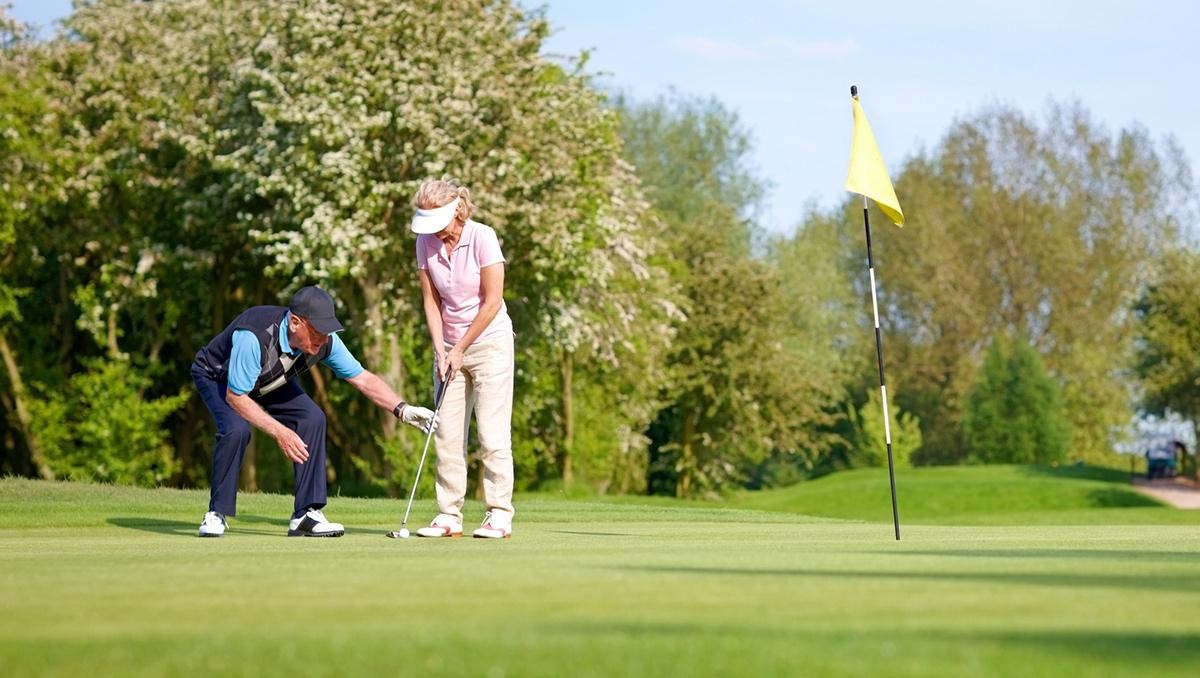 Senior golf trainer teaching the proper putting technique with woman at golf course