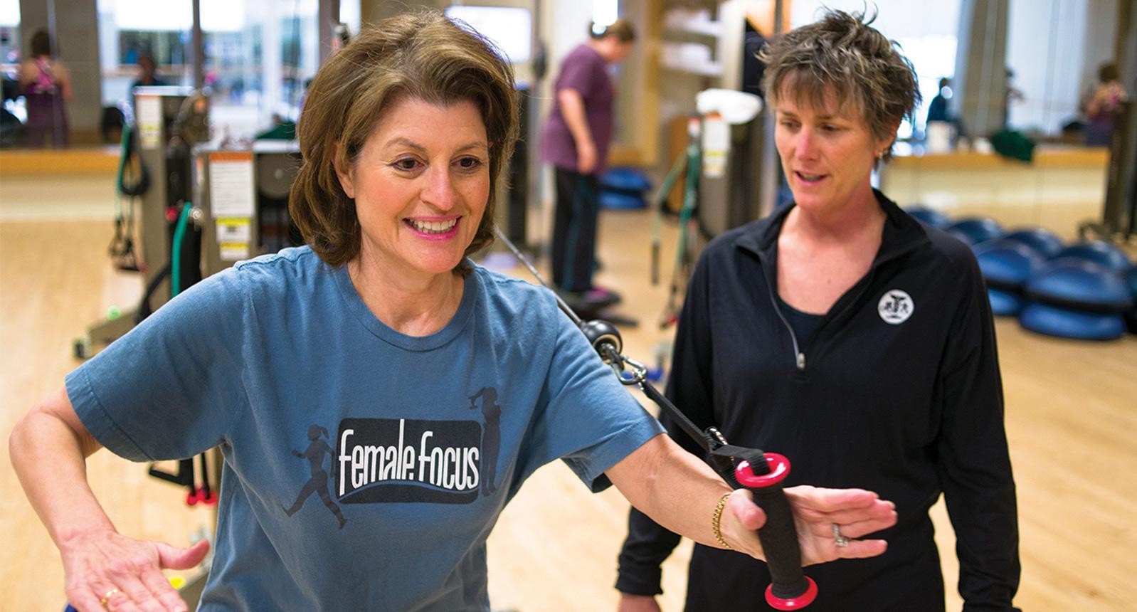 Woman wearing female focus Cooper t-shirt being trained by a Cooper fitness staff member