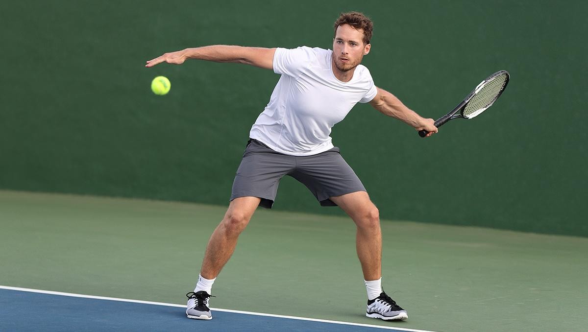 Man swinging on a tennis court about to hit a tennis ball