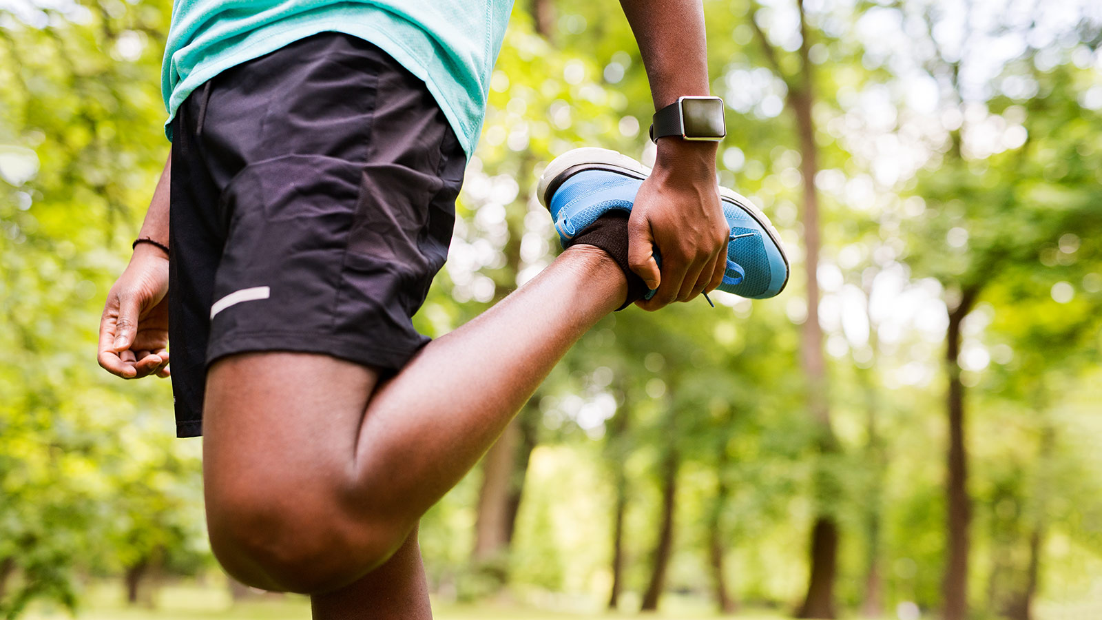 Unrecognizable afro-american man in park warming up and stretching arms and legs before training.