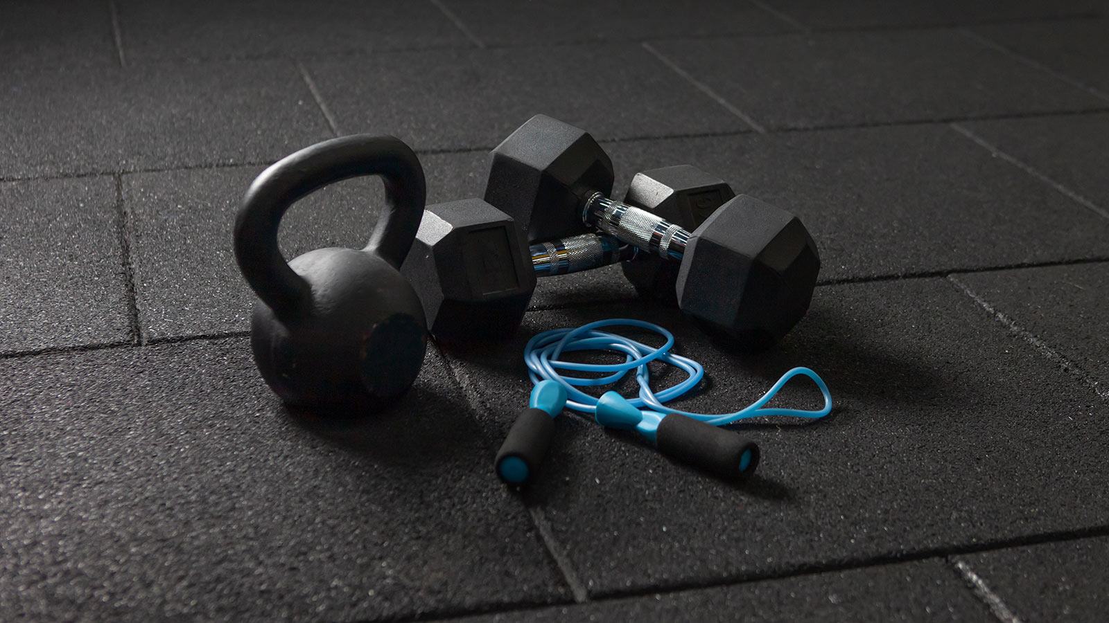 Functional training Sports equipment. Kettlebell and skipping rope, dumbbells on a dark black floor
