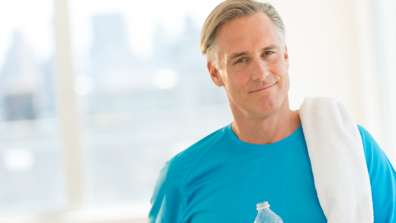 Portrait of confident mature man with towel and water bottle at health club