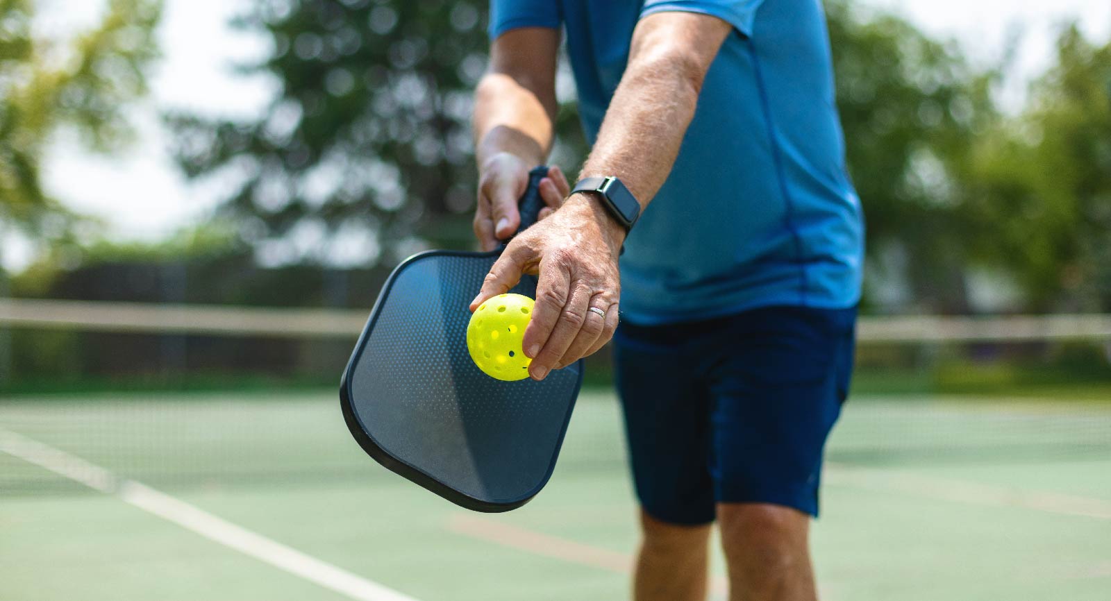 Person holding a Pickleball paddle and ball, ready to serve.