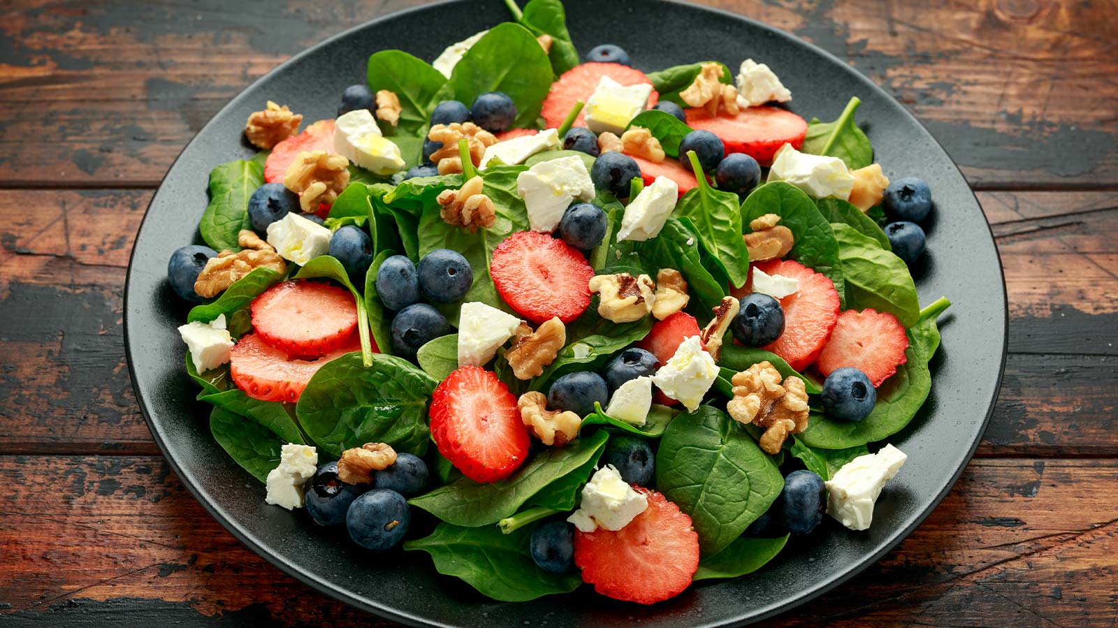 A bowl of spinach blueberry walnut and strawberry salad