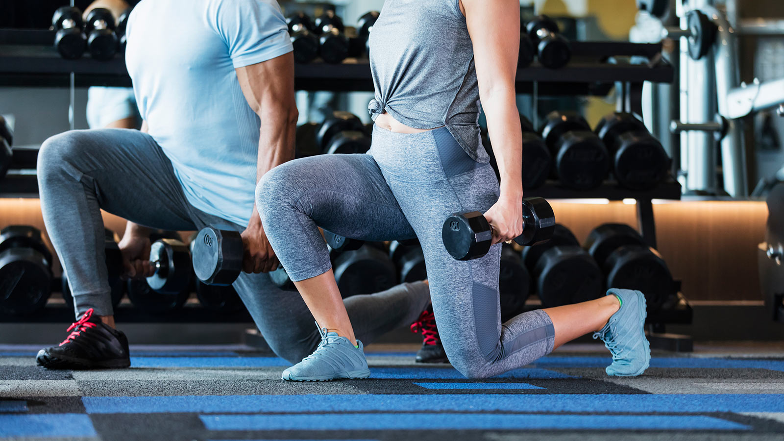 Profile view of a couple doing kneeling lunges with dumbbells at home