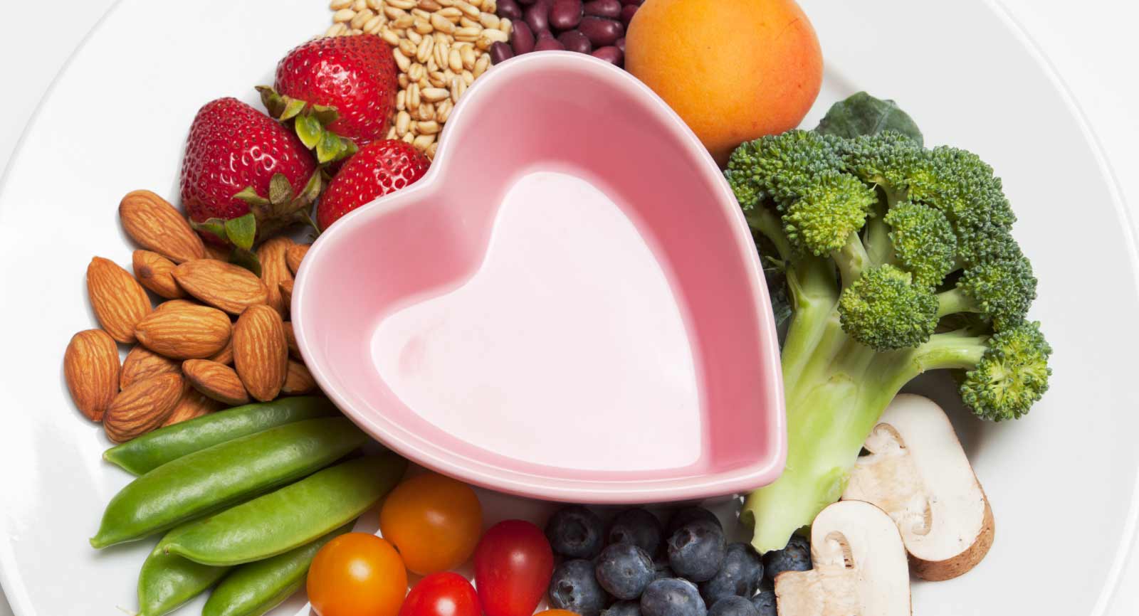 Pink heart bowl on a plate surrounded by fruits and vegetables