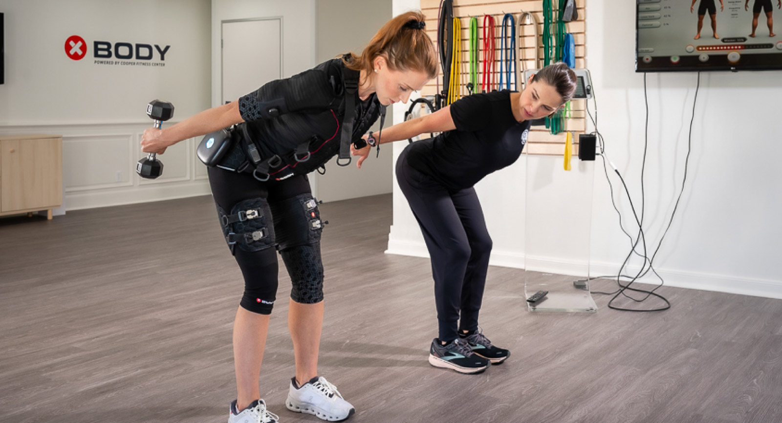 EMS fitness trainer works with client as she lifts weights
