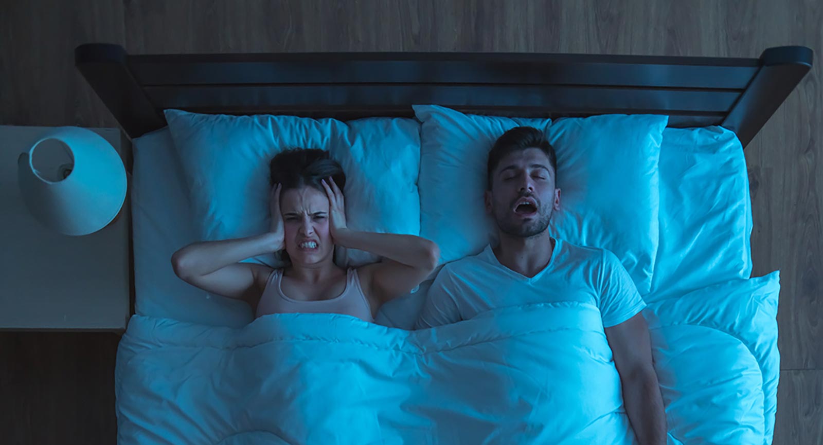 Man snoring and woman holding her ears in annoyance